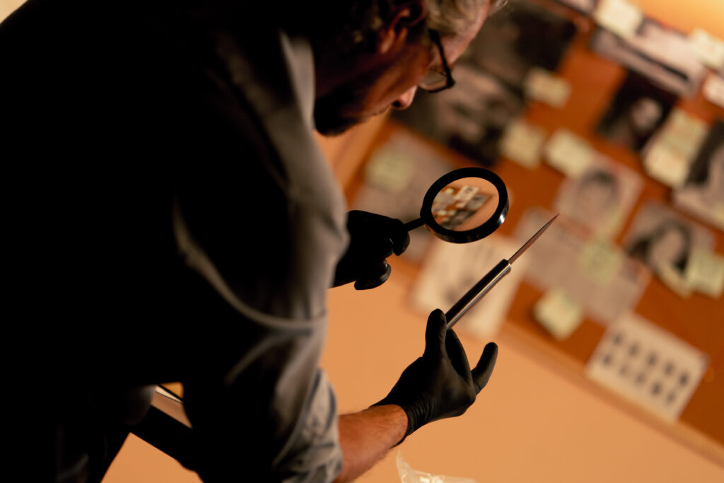 detective's office middle-aged investigator in shirt and tie sitting desk examining evidence bloody knife murder weapon